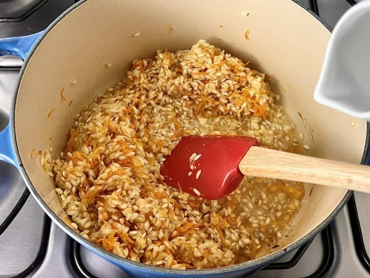 Uma panela contendo vegetais e arroz refogados com vinho branco.