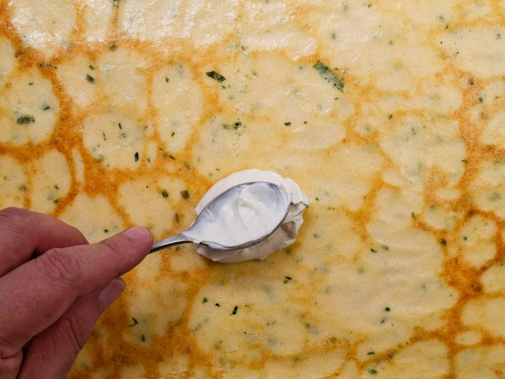 Requeijão sendo espalhado por uma colher sobre a massa assada e desenformada.