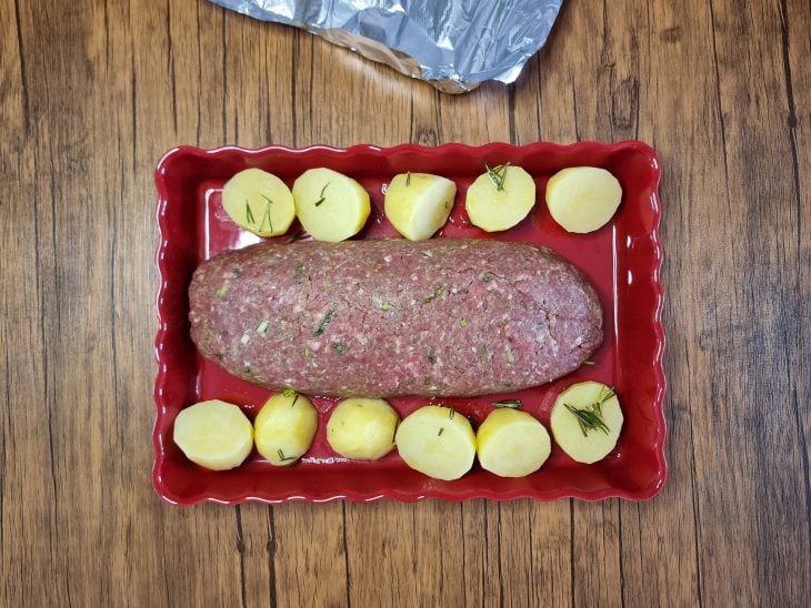 Rocambole de carne no meio da travessa com batatas cortadas ao lado.