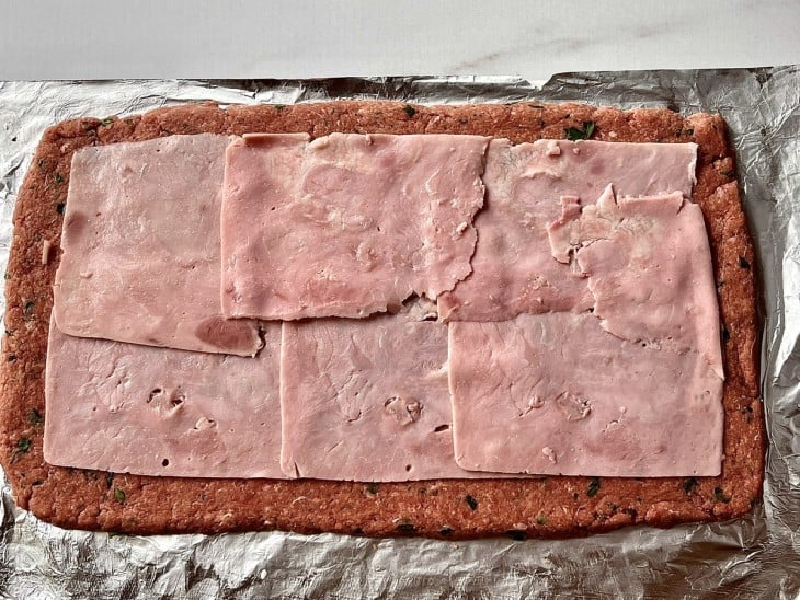 A massa de carne aberta recheada com fatias de presunto.