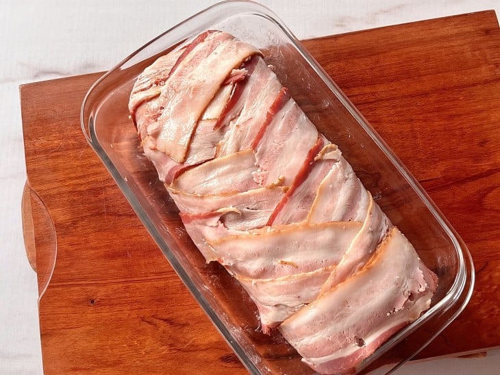 Um refratário contendo rocambole cru de carne moída com bacon.