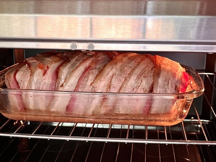 Um refratário contendo rocambole de carne moída com bacon no forno.