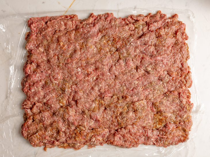 Carne disposta, de forma retangular, sobre um plástico filme.