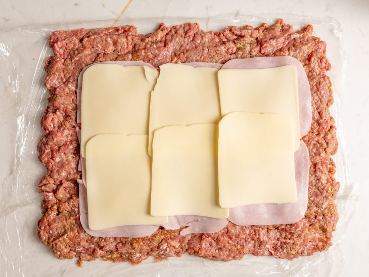 Fatias de presunto e mussarela sobre a carne.