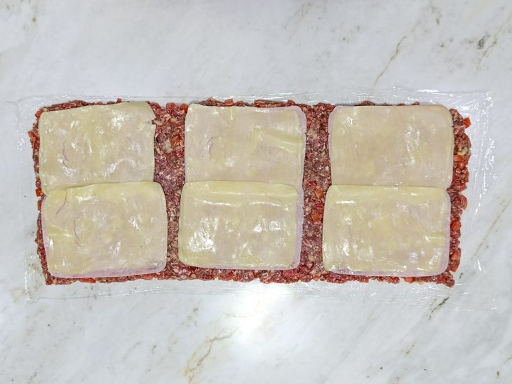 Fatias de queijo colocadas sobre a camada de carne.