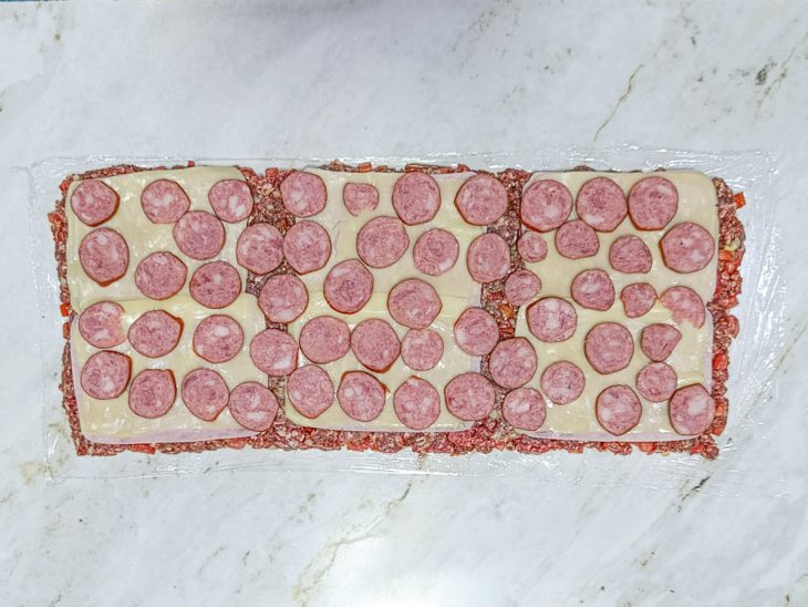 Rodelas de calabresa colocadas sobre as fatias de queijo.