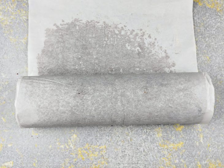 Massa do rocambole sendo enrolada com ajuda do papel-manteiga.