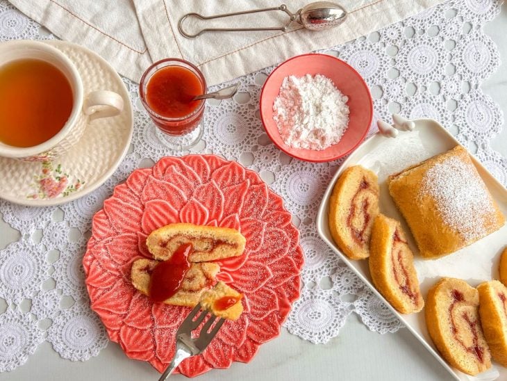 Prato finalizado com açúcar confeiteiro e uma xícara de chá ao lado.