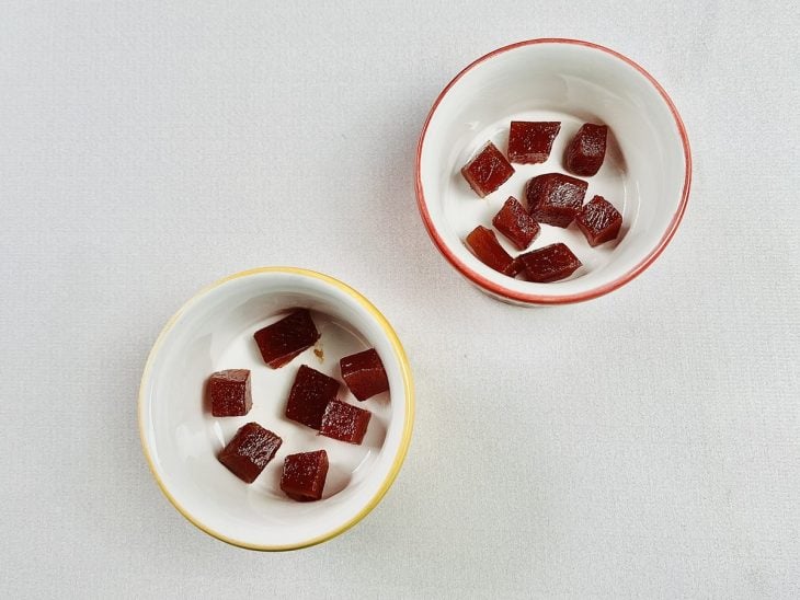 Pequenos potes de porcelana com cubos de goiabada ao fundo.