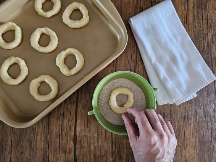 Uma rosquinha sendo passada na mistura de açúcar e canela.