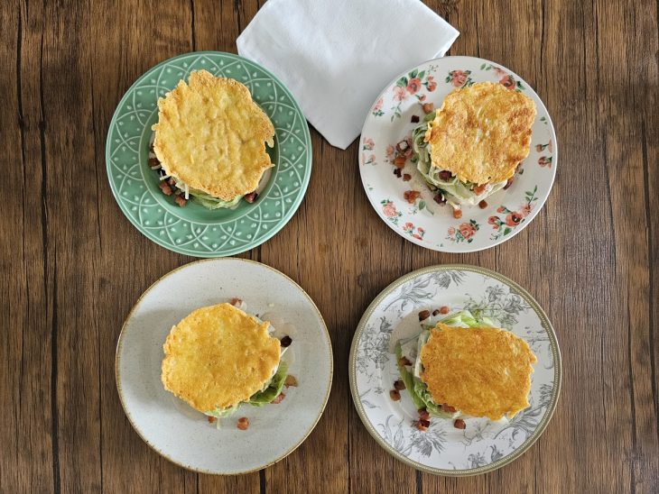 Quatro pratos com salada Caesar com crispy de queijo montadas.