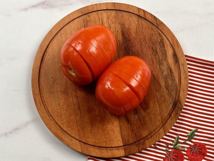 Uma tábua contendo dois tomates fatiados, mas sem chegar à base.