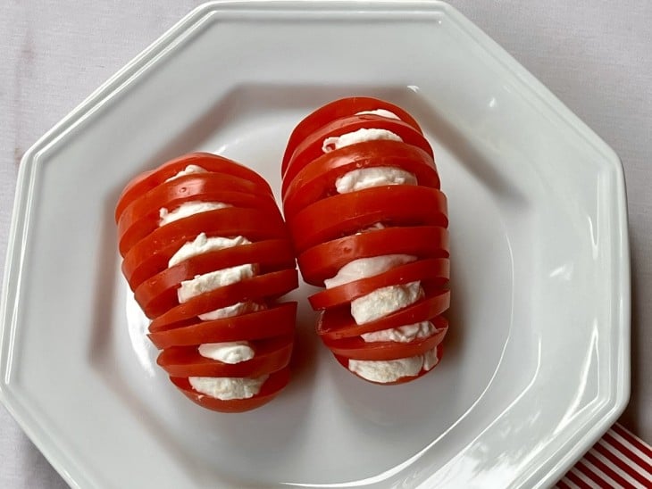 Um prato contendo dois tomates fatiados com mussarelas de búfalas entre as fatias.