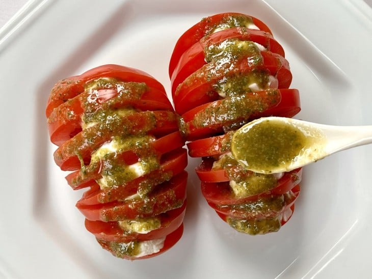 Um prato contendo dois tomates fatiados com mussarelas de búfalas e molho pesto.