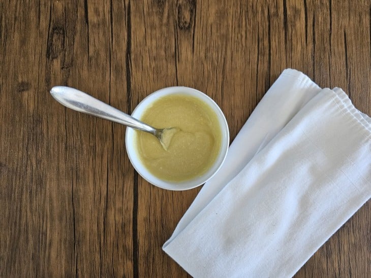 Molho da salada colocado em um potinho branco e uma colher.