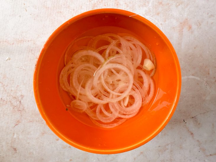 Cebola em rodelas sendo colocada em tigela com água.