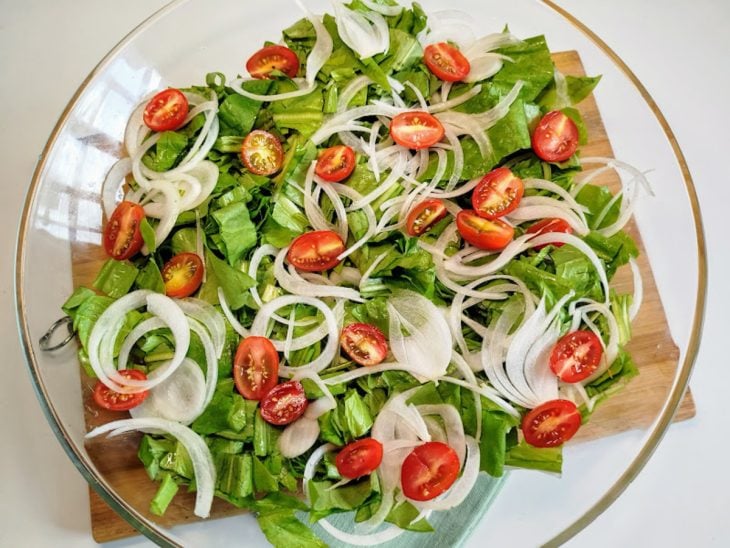 Um recipiente com almeirão, tomates-cereja e cebolas picadas.