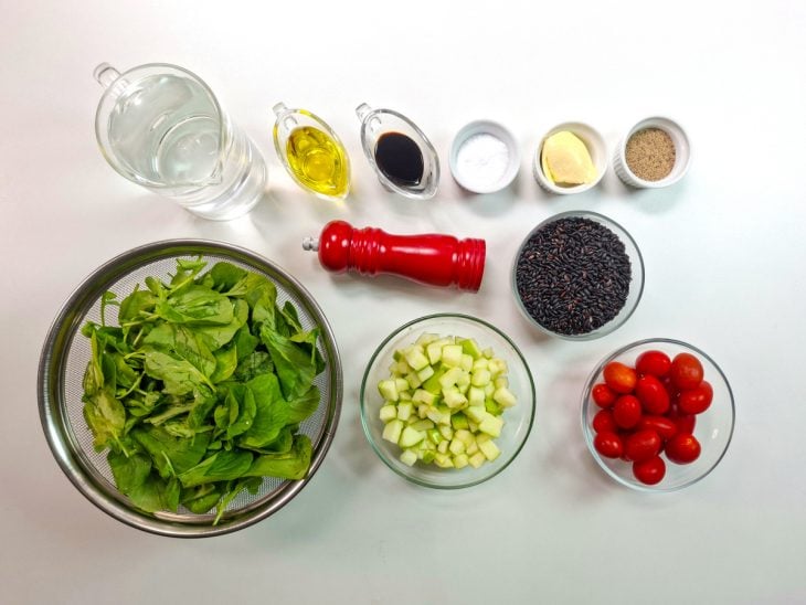 Ingredientes organizados na bancada com arroz negro, frutas, folhas e temperos.