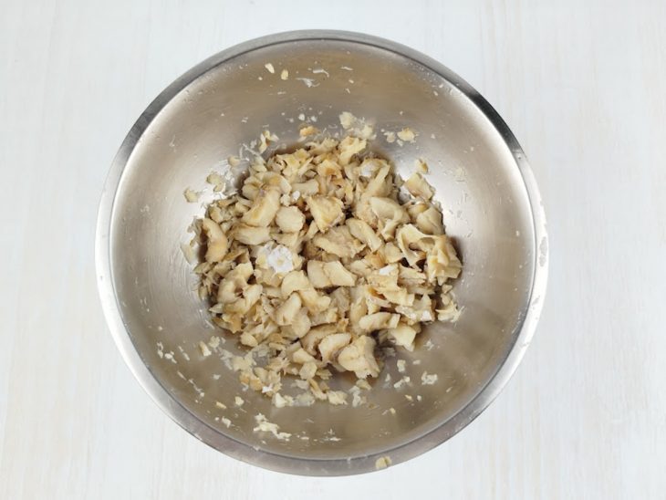 Bacalhau desfiado em tigela com ajuda de garfo.