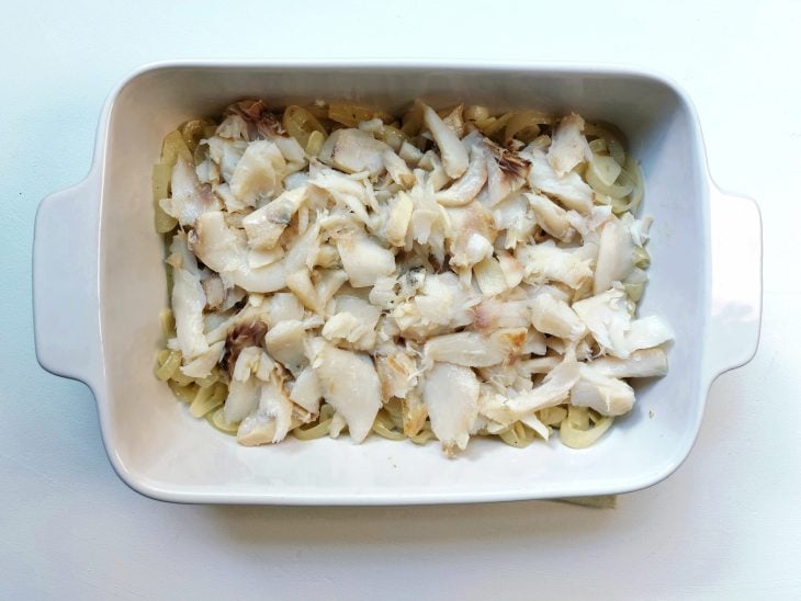 Refratário com ingredientes assados e bacalhau desfiado por cima.