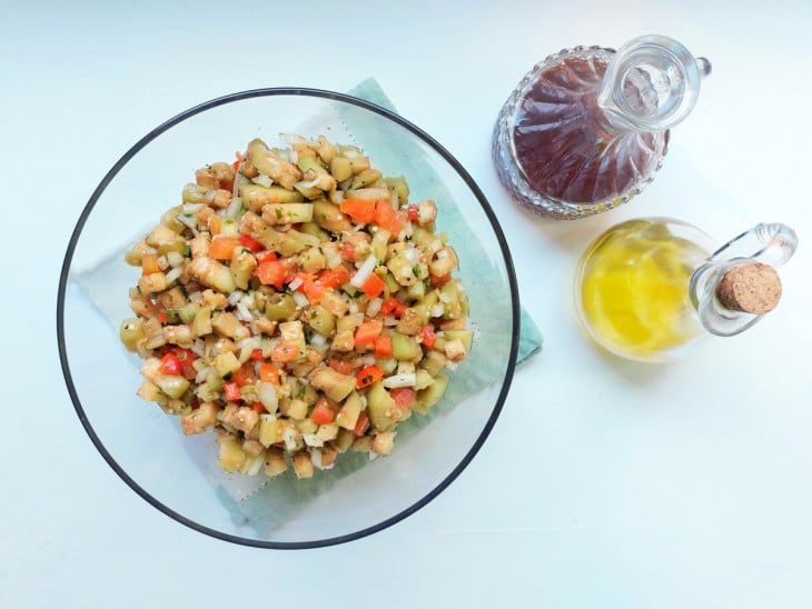 Salada de berinjela crua com vinagre e azeite em recipientes ao lado.