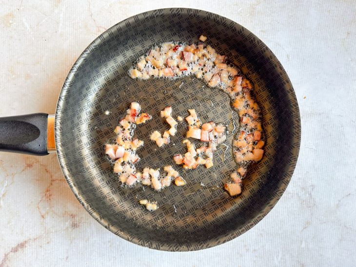 Bacon em cubos sendo frito até dourar e ficar crocante.