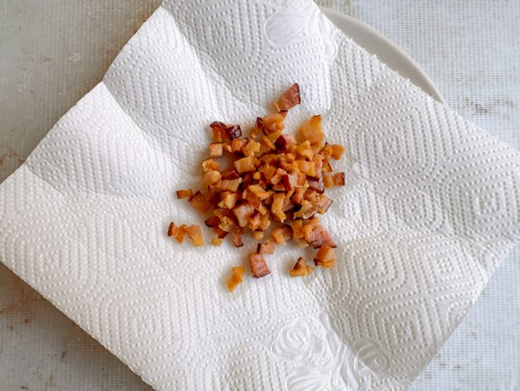Bacon escorrendo sobre papel toalha para retirar o excesso de gordura.