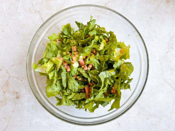 Chicória sendo misturada com o bacon e o molho na tigela.