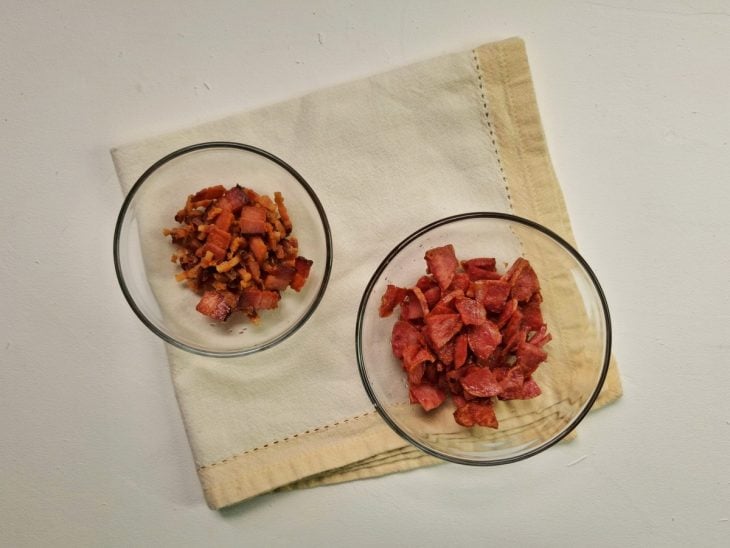 Linguiça e bacon picadinhos e fritos em recipientes separados.