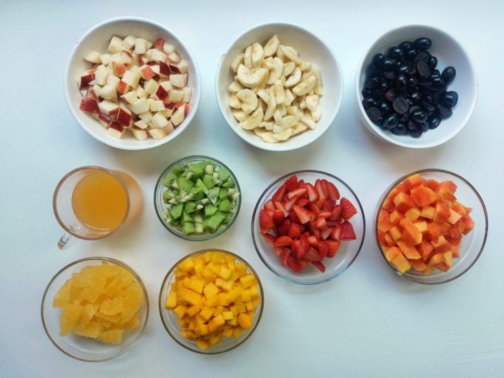 Uma bancada com recipientes contendo as frutas picadas e o suco de laranja.