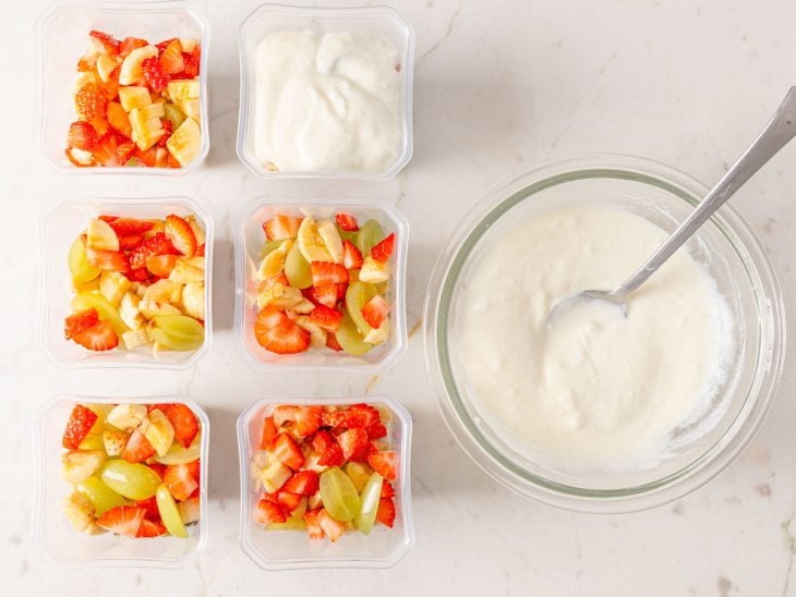 Potinhos de salada de frutas sendo montados.