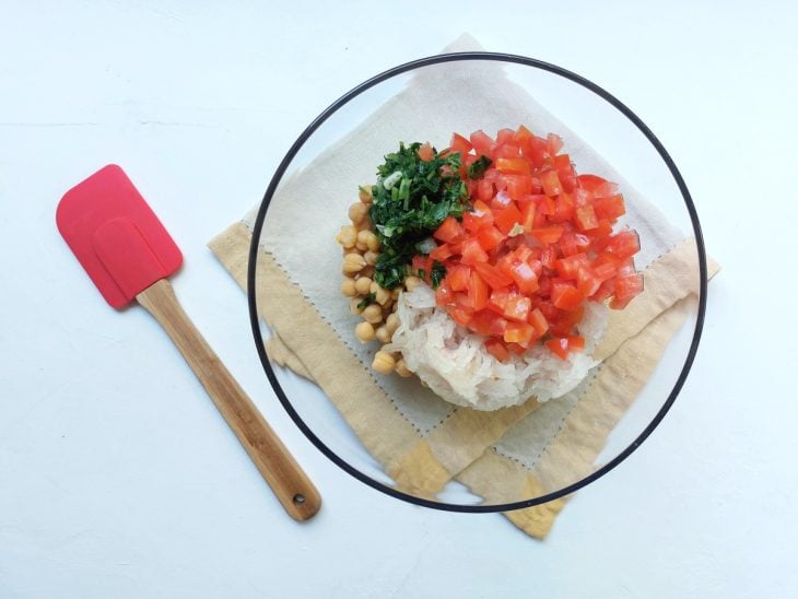 Grão-de-bico, tomate, cebola e salsinha adicionados em uma tigela.