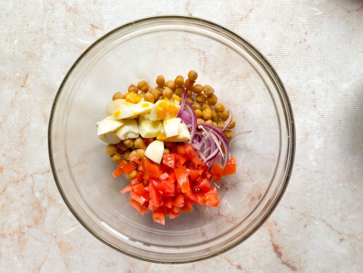 Numa tigela, o grão-de-bico, os ovos, os tomates e a cebola roxa.