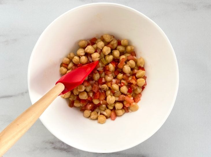 Uma tigela contendo grão-de-bico, cebola, tomate, sal, azeite, suco de limão e pimentão picado.