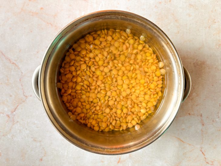 Grãos de lentilha cobertos por água numa panela.