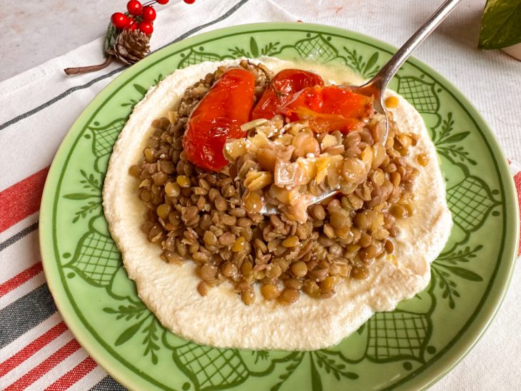 Salada de lentilha com tomates e molho de ricota servida em um prato individual, com uma porção destacada numa colher de sopa.