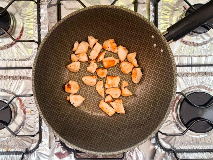 Frigideira no fogão, com os cubos de frango grelhados.