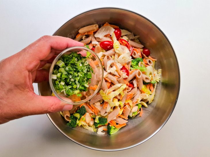 Ao fundo, tigela com os ingredientes misturados, em foco o cheiro verde sendo adicionado a mistura.