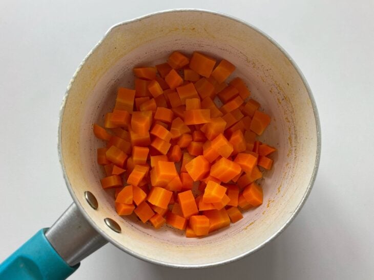 Cubos de pepino sem sementes polvilhados com sal descansando dentro de um escorredor de inox.