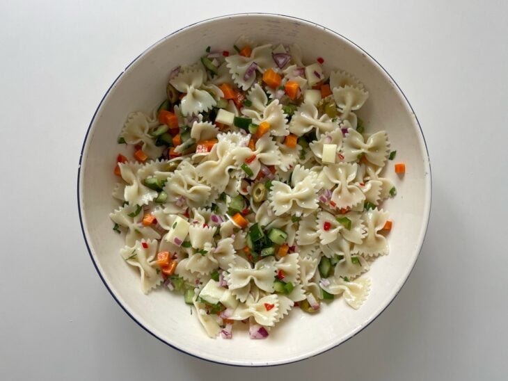 Salada de macarrão finalizada e colorida sendo transferida da tigela para uma travessa de servir.