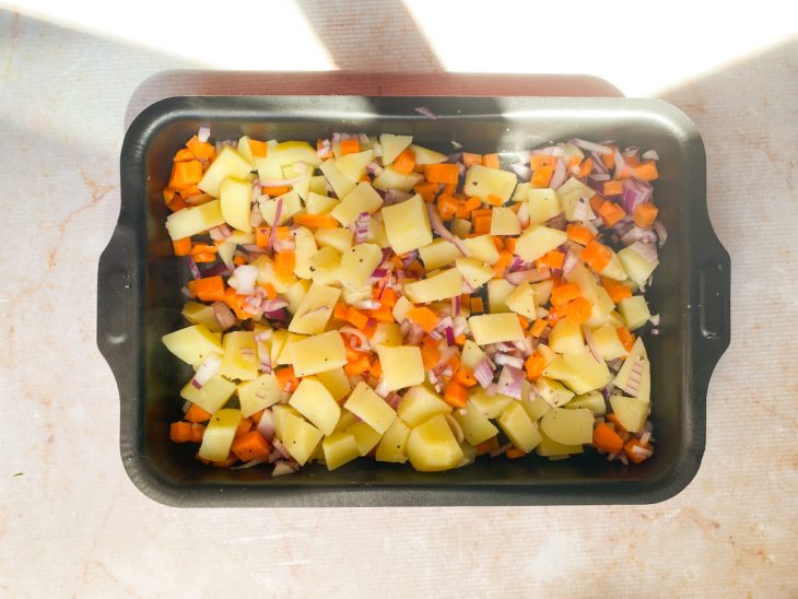 Na assadeira, as batatas cozidas, as cenouras e a cebola crua.