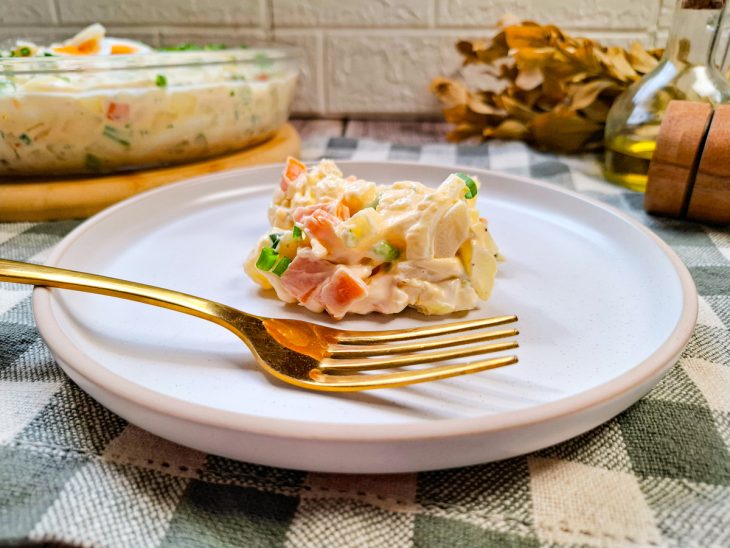 Porção da salada servida em prato, uma garfo em primeira plano completa o quadro.