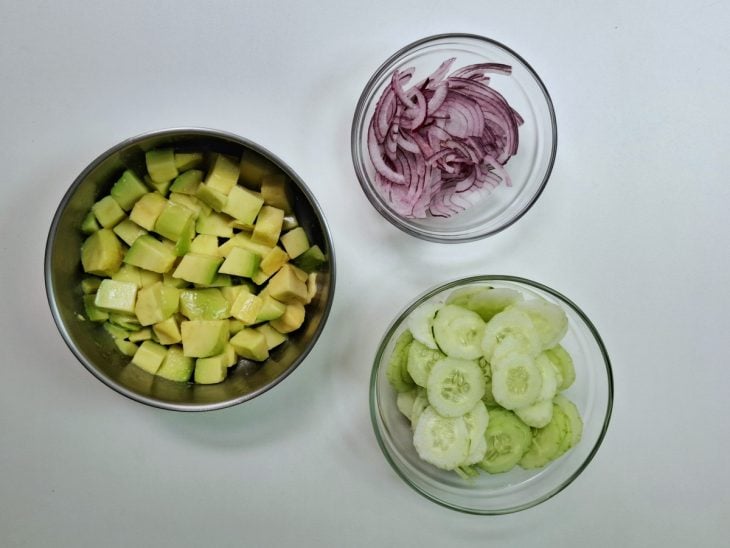 Abacate, cebola roxa e pepino cortados em pequenos potes separados.