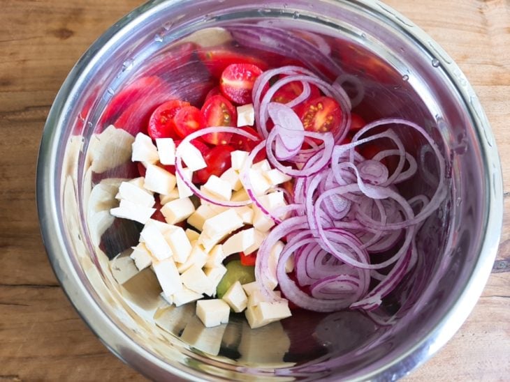 Uma tigela com pepino, queijo, tomates e cebola.