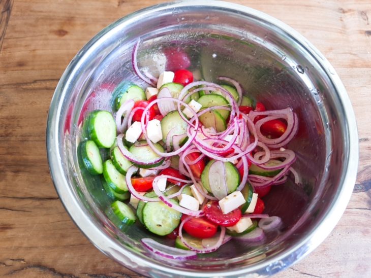 Um recipiente contendo salada de pepino e tomate-cereja.