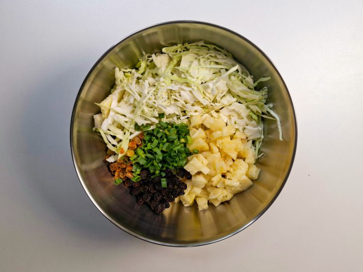 Repolho, abacaxi, uvas-passas e cebolinha misturados na tigela.