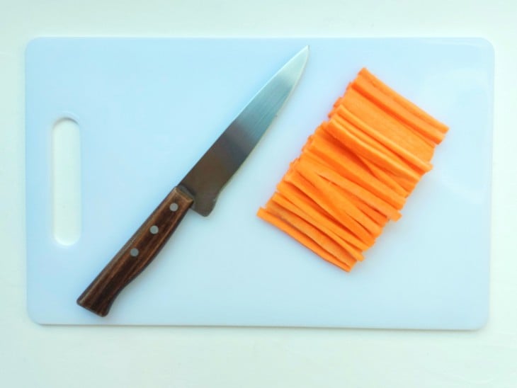 Cenoura cortada em tiras em uma tábua com faca ao lado.