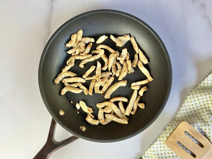 Uma frigideira com tiras de frango, azeite e temperos.