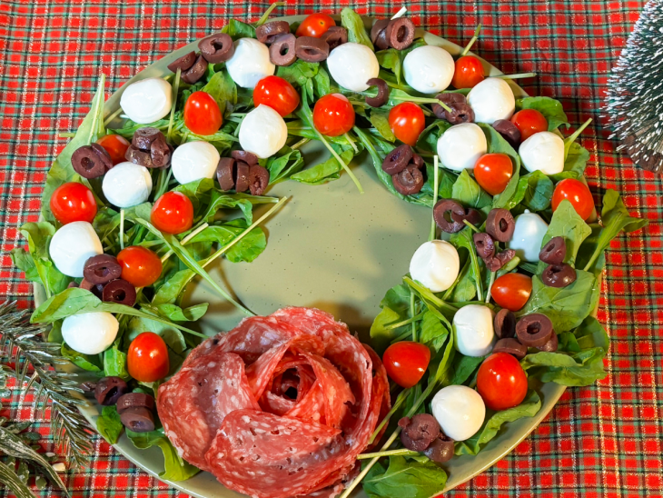 Tomatinhos, azeitonas e bolinhas de mussarela sendo posicionadas sobre as folhas