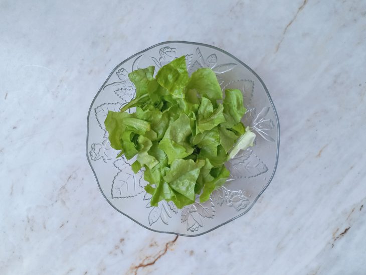 Folhas de alface rasgadas em pedaços rústicos sobre uma travessa.